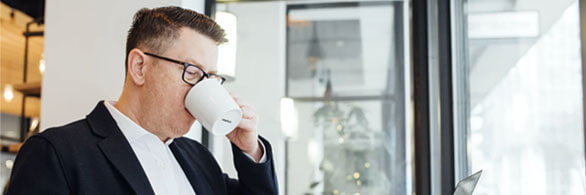 Man in suit drinking coffee by window.