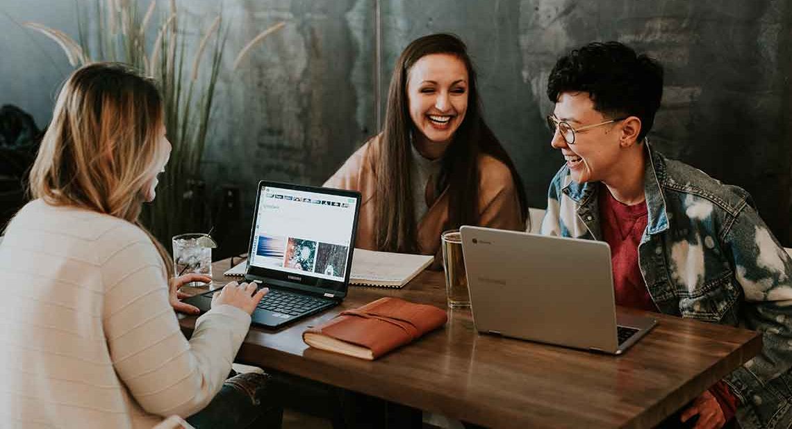 Three friends working on laptops and smiling.