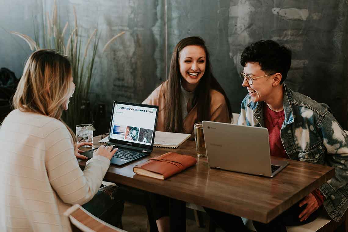 Three friends working on laptops and smiling.