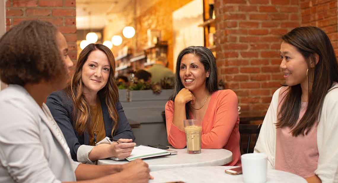 Four women chat at a cafe table.