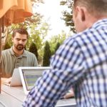 Two men working on laptops outdoors.