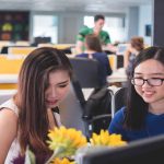 Two women working at a computer in an office.