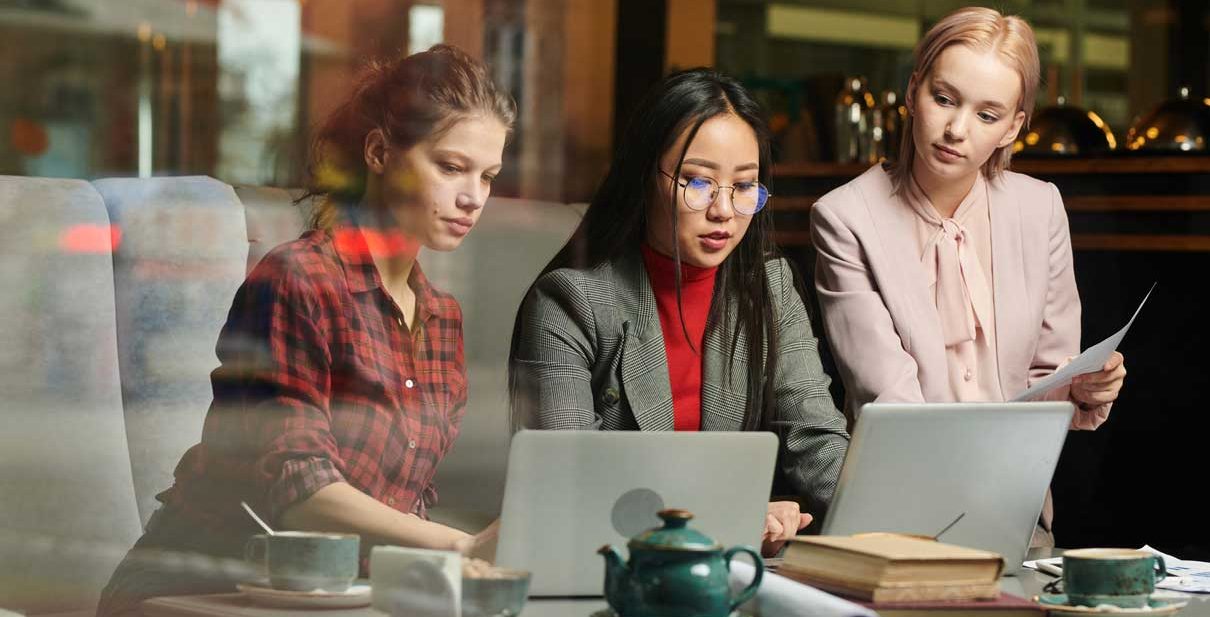 Three women working on laptops in cafe.