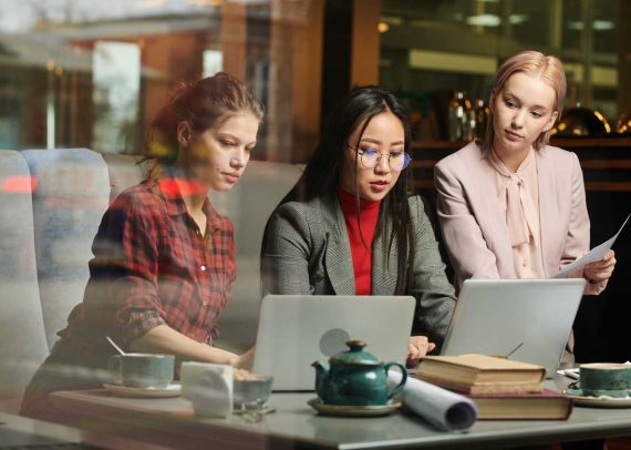 Three women working on laptops in cafe.