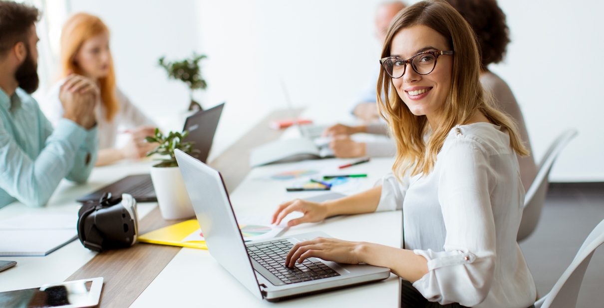 Woman smiling, typing on laptop in office.