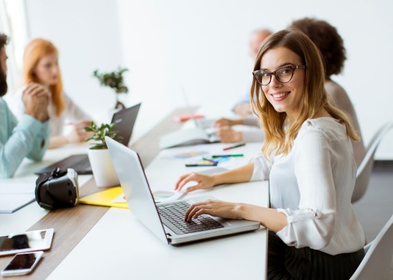 Woman smiling, typing on laptop in office.