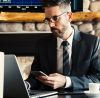 Businessman working on laptop with phone.