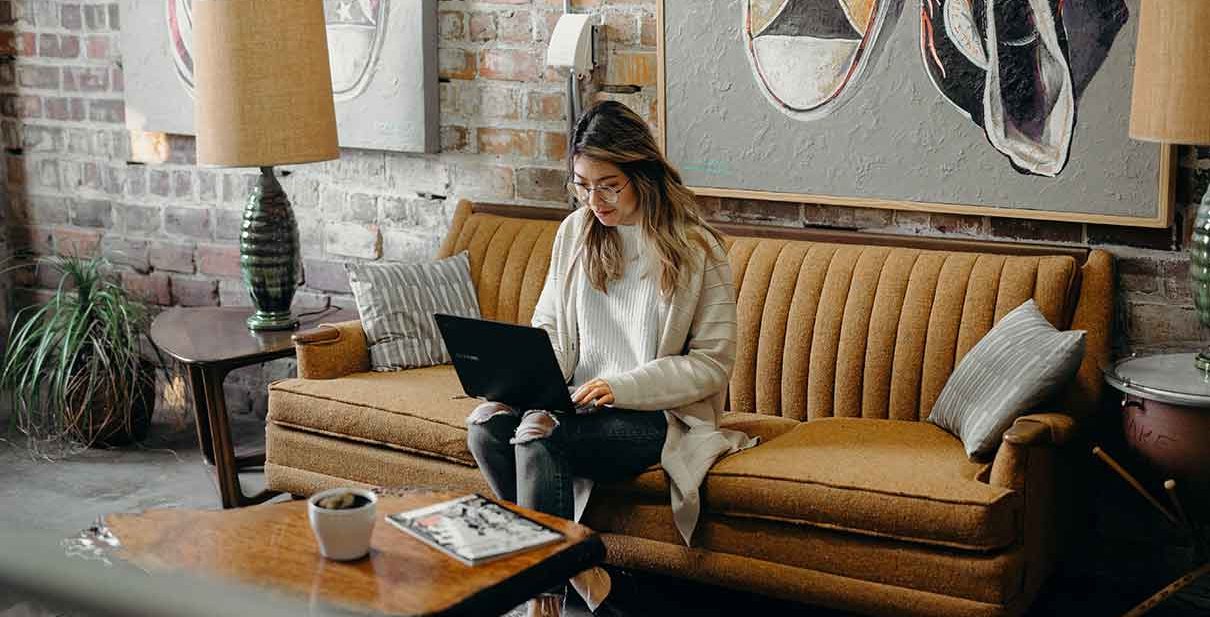 Woman working on laptop on a couch.