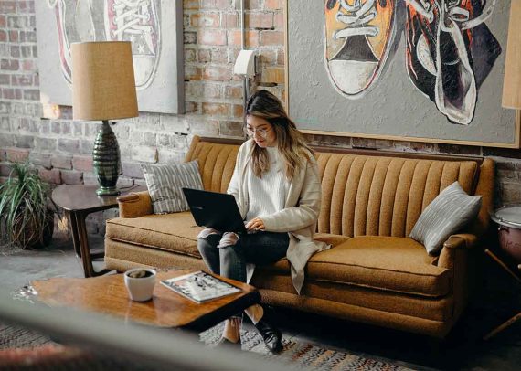 Woman working on laptop on a couch.