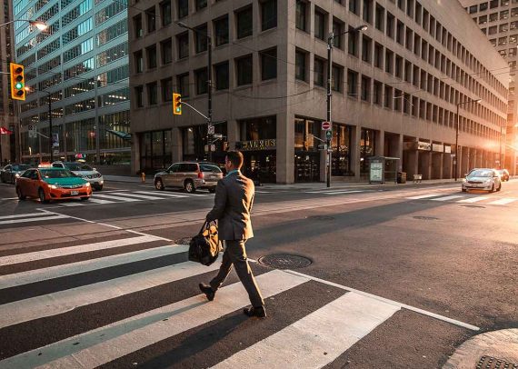 Man crossing city street with bag.