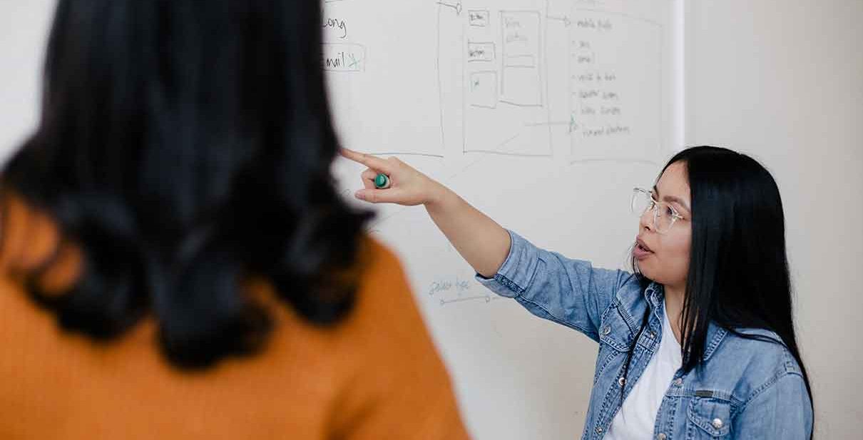 Woman explaining a whiteboard to another person.