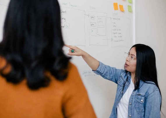 Woman explaining a whiteboard to another person.