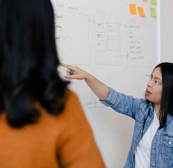 Woman explaining a whiteboard to another person.