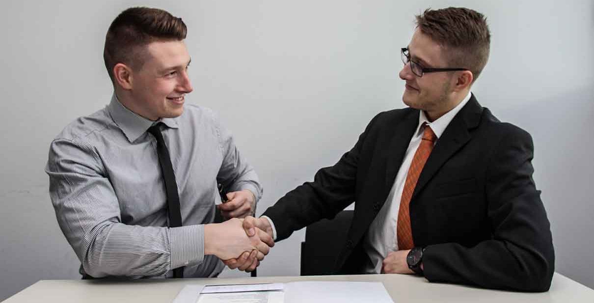 Two men shaking hands at a desk.