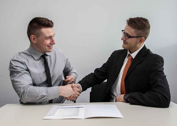 Two men shaking hands at a desk.