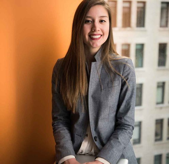 Smiling woman in grey blazer holding a laptop.