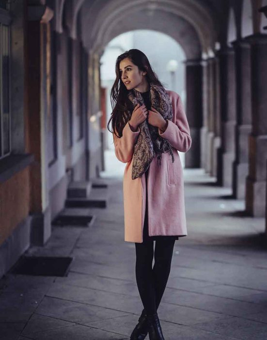 Woman in pink coat standing in alleyway.