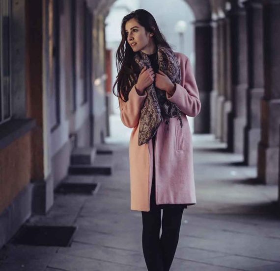 Woman in pink coat standing in alleyway.