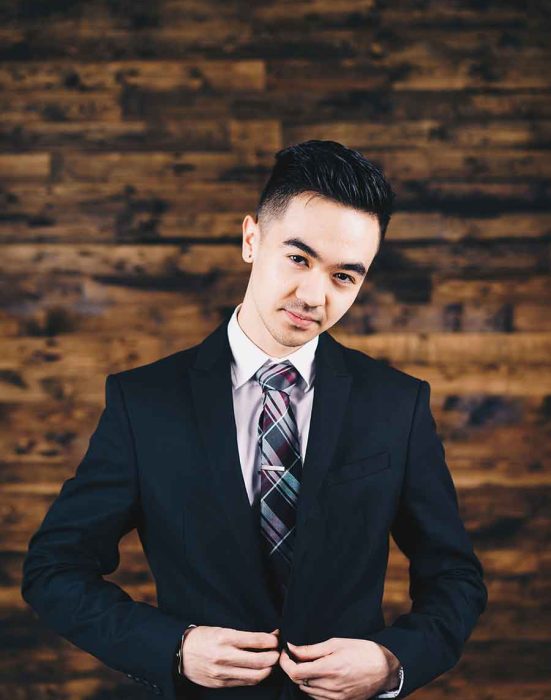 Man in suit adjusts tie against wood wall.