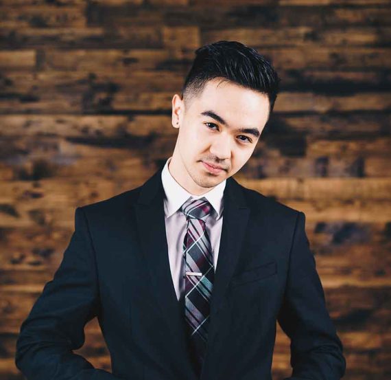 Man in suit adjusts tie against wood wall.