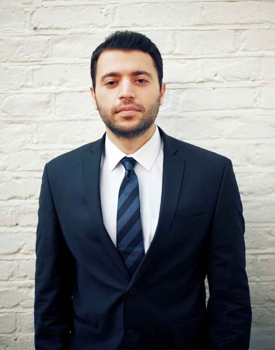 Man in a suit and tie against white brick wall.