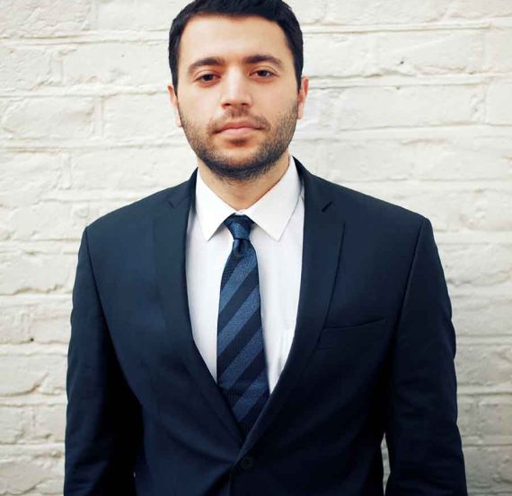 Man in a suit and tie against white brick wall.