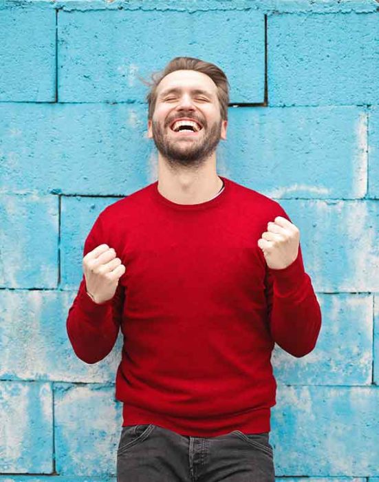 Man in red sweater smiles against blue wall.