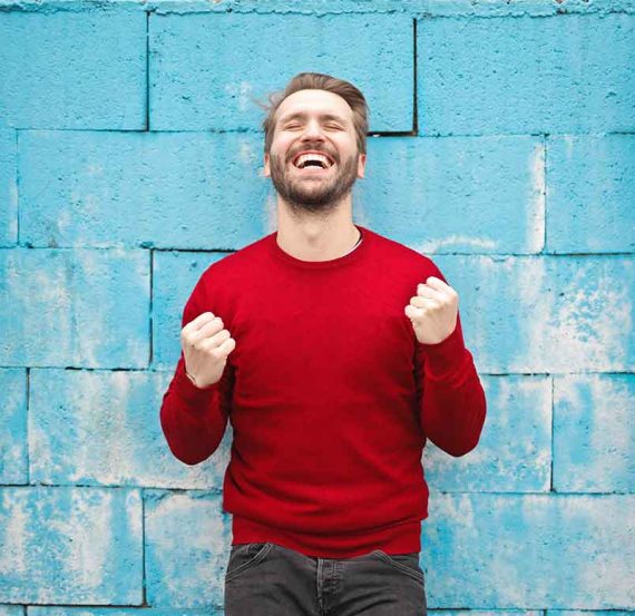 Man in red sweater smiles against blue wall.