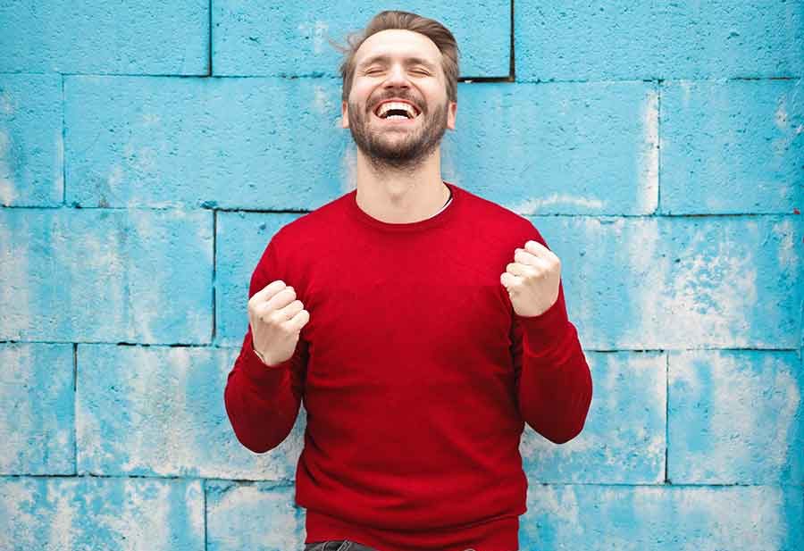 Man in red sweater smiles against blue wall.