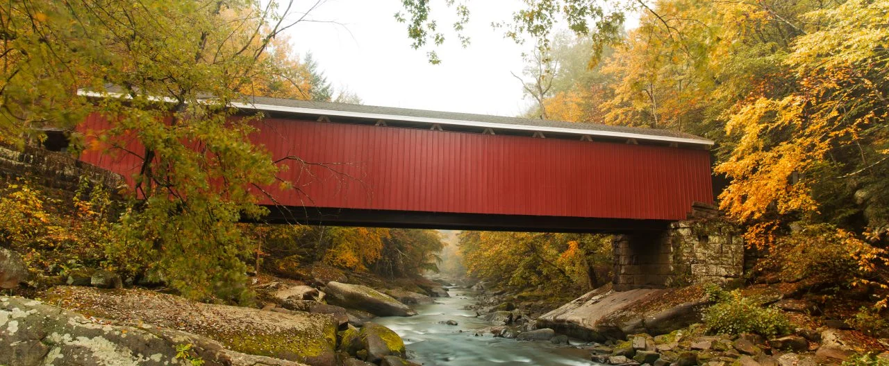 Red covered bridge over a stream in autumn.