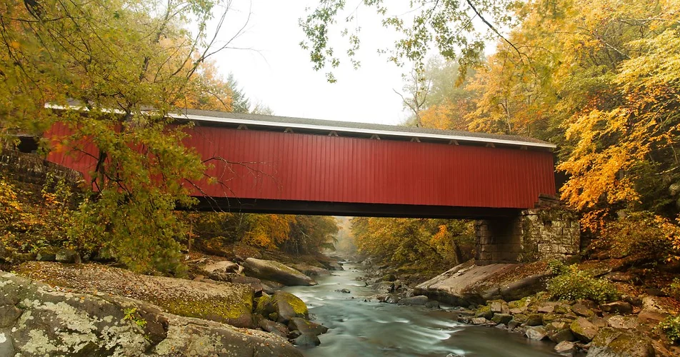 Red covered bridge over a river in autumn.