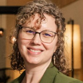 A smiling woman with curly hair and glasses.