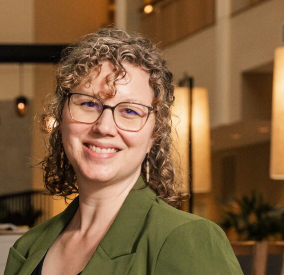 Smiling woman with curly hair wearing glasses.