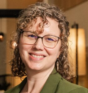 A woman with curly hair and glasses smiles.